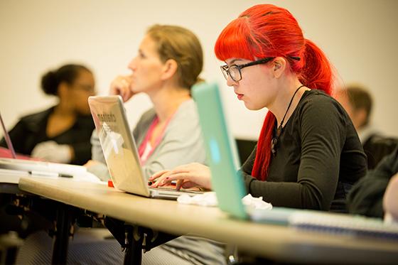 照片上，一个戴着眼镜、一头鲜红头发的学生在课堂上用笔记本电脑打字