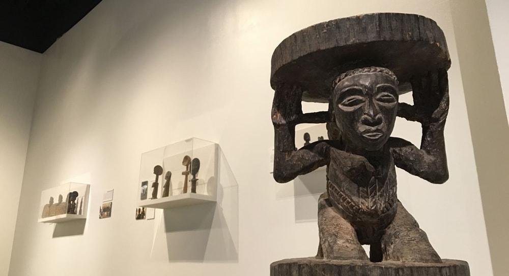一个非洲雕塑的照片，一个人头上顶着一个盘子，在画廊里