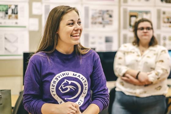 图为一名身穿紫色波胆网站衬衫的女学生在教室里微笑.